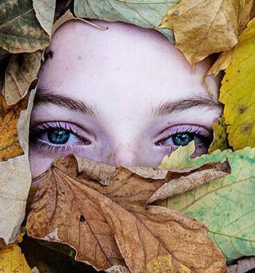 Augen einer Frau blicken aus einem Blätterberg heraus